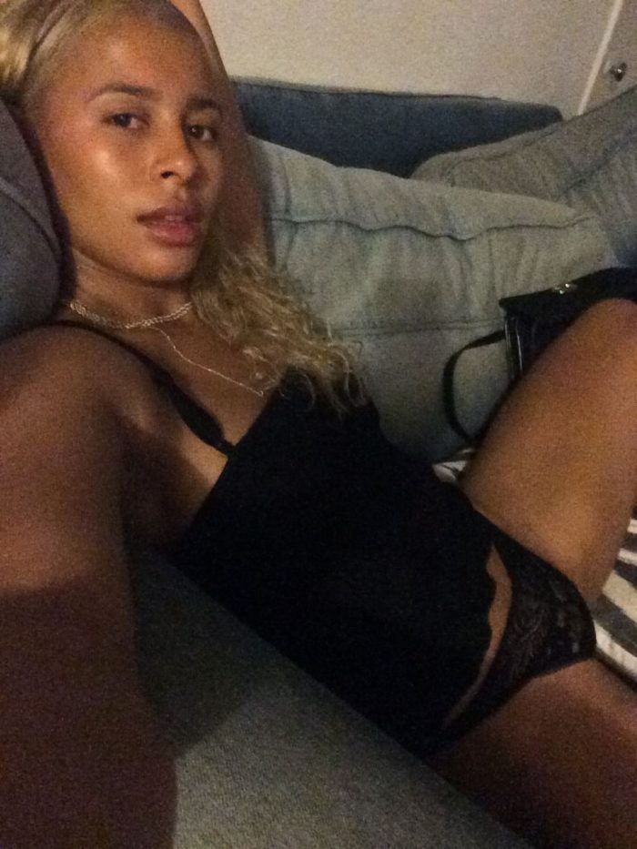 Sami Miro wearing a black top and underwear sitting on couch